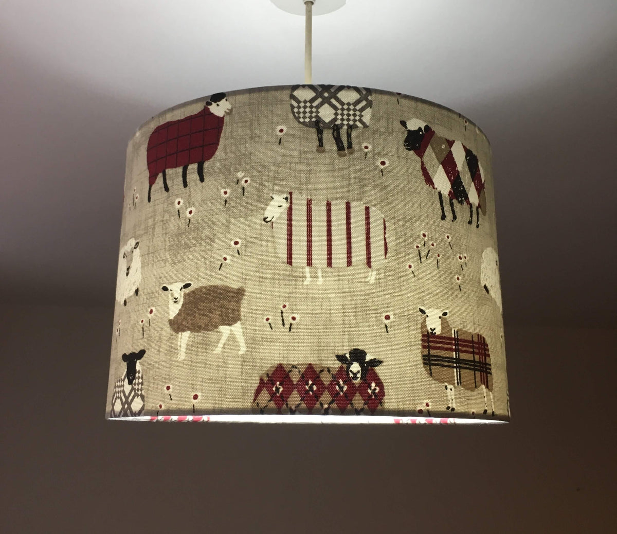 Fabric drum ceiling lampshade with sheep pattern on a plain background.
