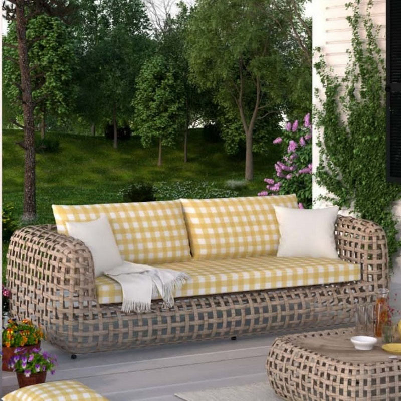 An outdoor patio featuring a wide, low-profile woven wicker sofa with yellow and white gingham checkered cushions