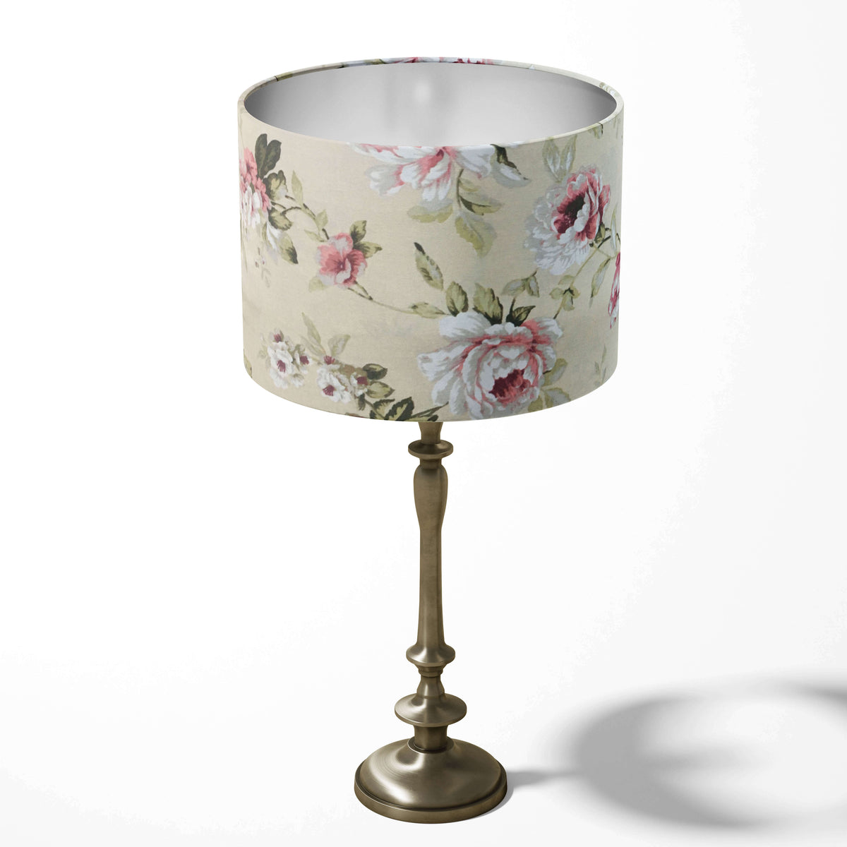 Pink floral-patterned beige table lampshade on a decorative stand against a white background.