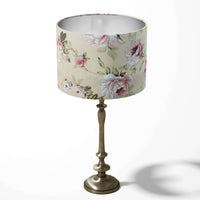 Pink floral-patterned beige table lampshade on a decorative stand against a white background.