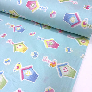 Cotton poplin fabric with colourful birdhouse, butterfly, bird and heart pattern on a light blue background.