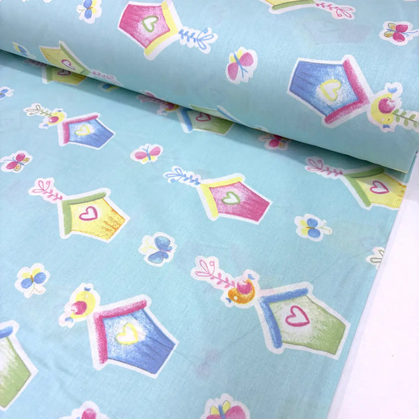 Cotton poplin fabric with colourful birdhouse, butterfly, bird and heart pattern on a light blue background.