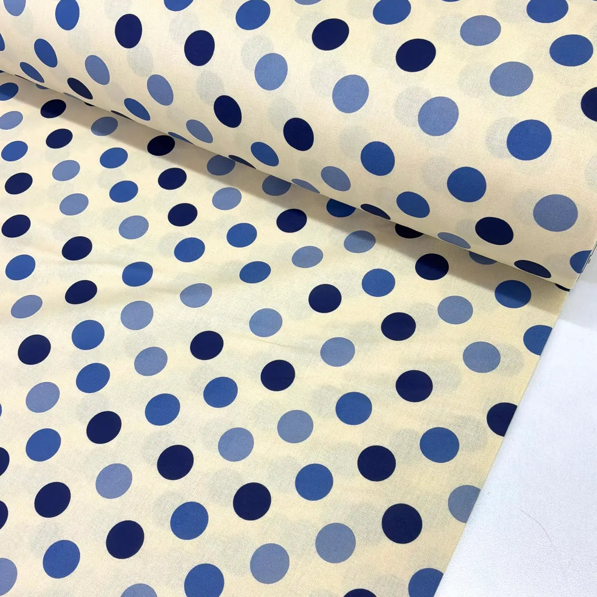 Blue polka dot cotton fabric with navy and cornflower blue spots on a cream background, ideal for dressmaking, quilting, patchwork and craft projects.
