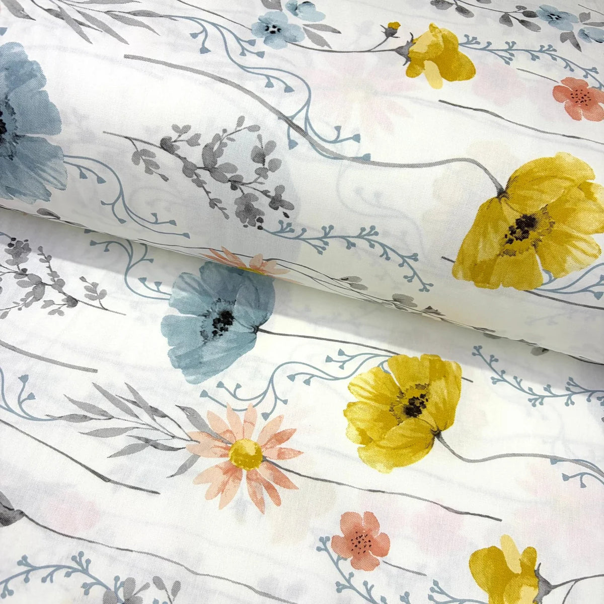 A white cotton poplin fabric with a watercolour floral print featuring yellow poppies, blue flowers, peach blossoms, and gray leaves on delicate stems.