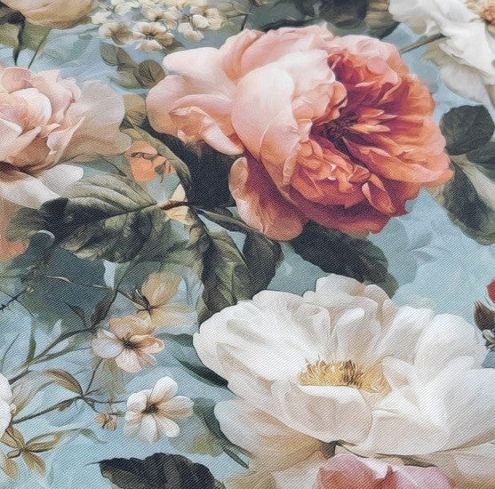 Close-up of an upholstery fabric patterned with pink and white flowers with green leaves on a light blue background.