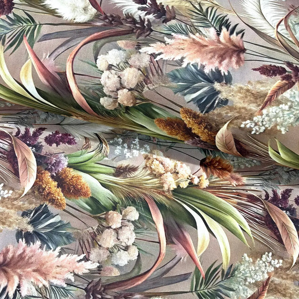 Botanical cotton fabric featuring pampas grass, tropical leaves and dried floral stems in neutral green, cream and blush tones on a taupe background.