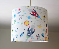 Children's lampshade with space-themed design featuring planets, rockets, sun, stars, and galaxy on a plain background.