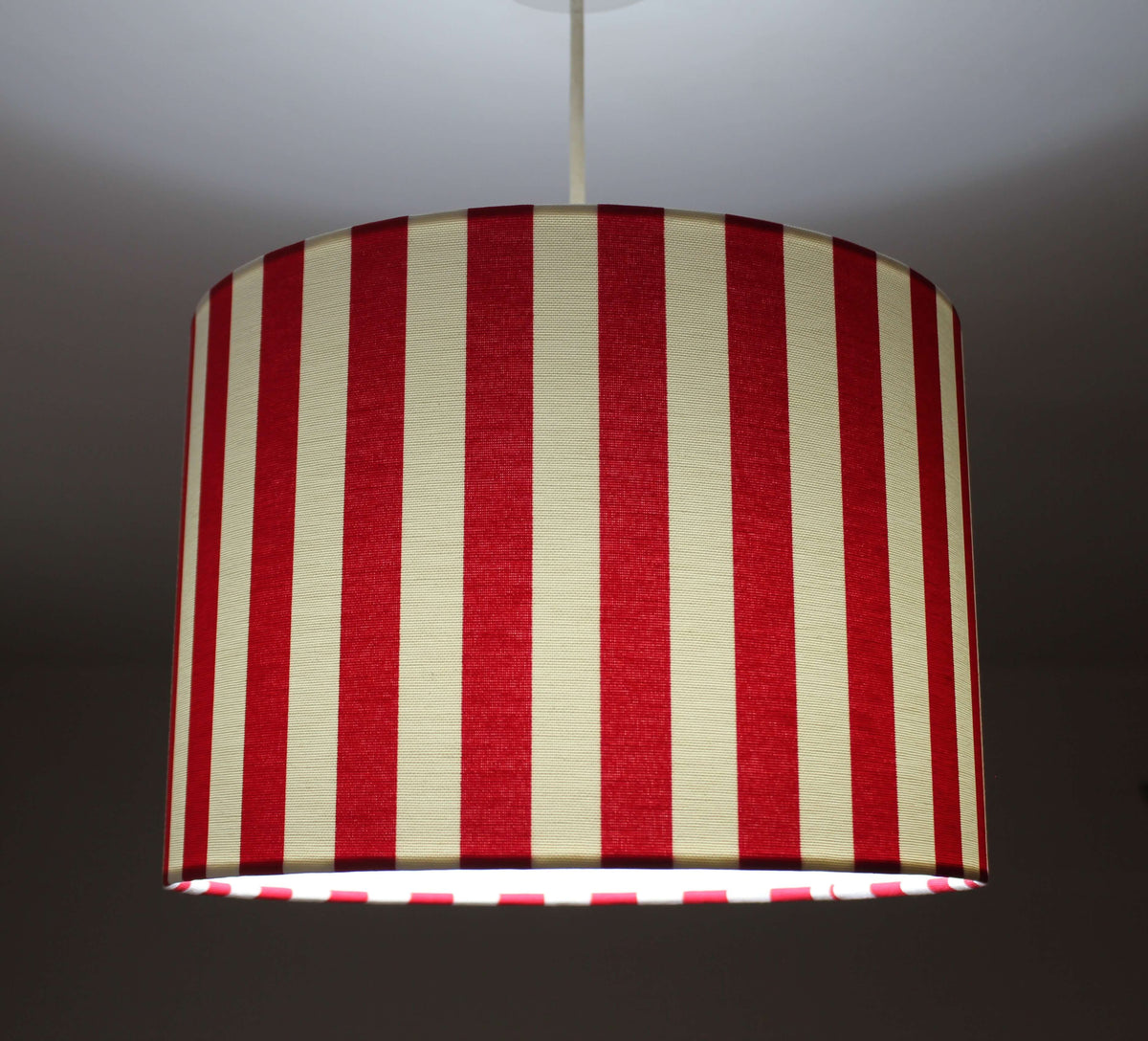 Modern striped bright red and white ceiling drum lampshade on a dark background.