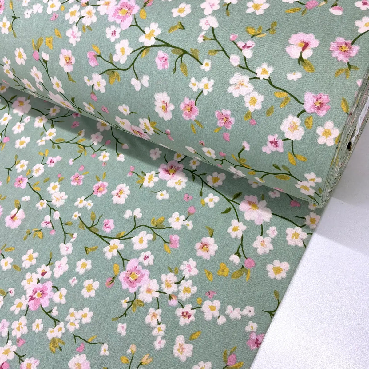 Cherry blossom floral cotton fabric featuring delicate pink and white flowers on a sage green background.