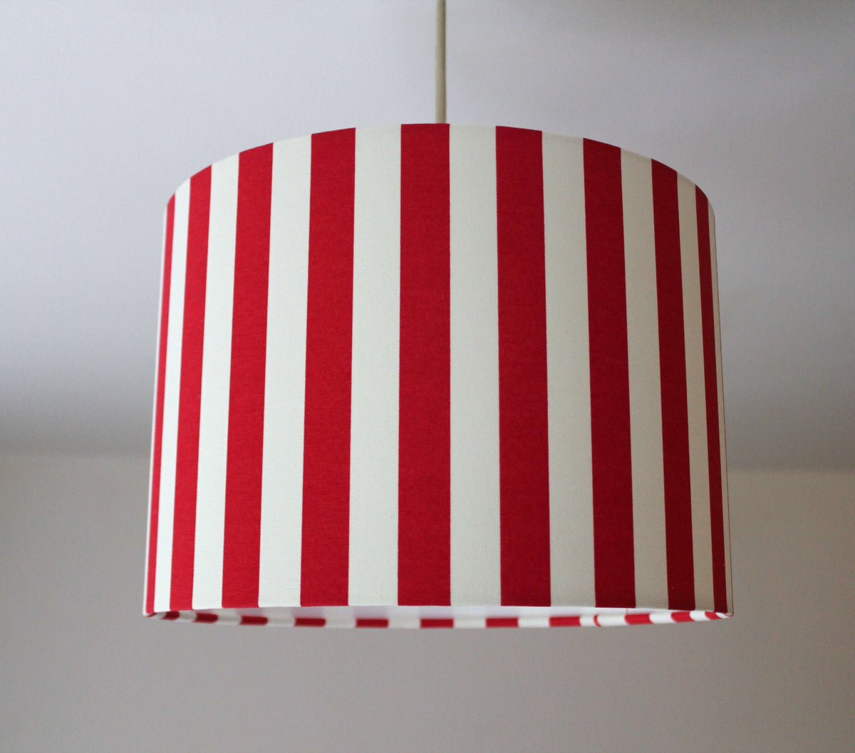 Red and white striped ceiling lampshade hanging on a plain background.