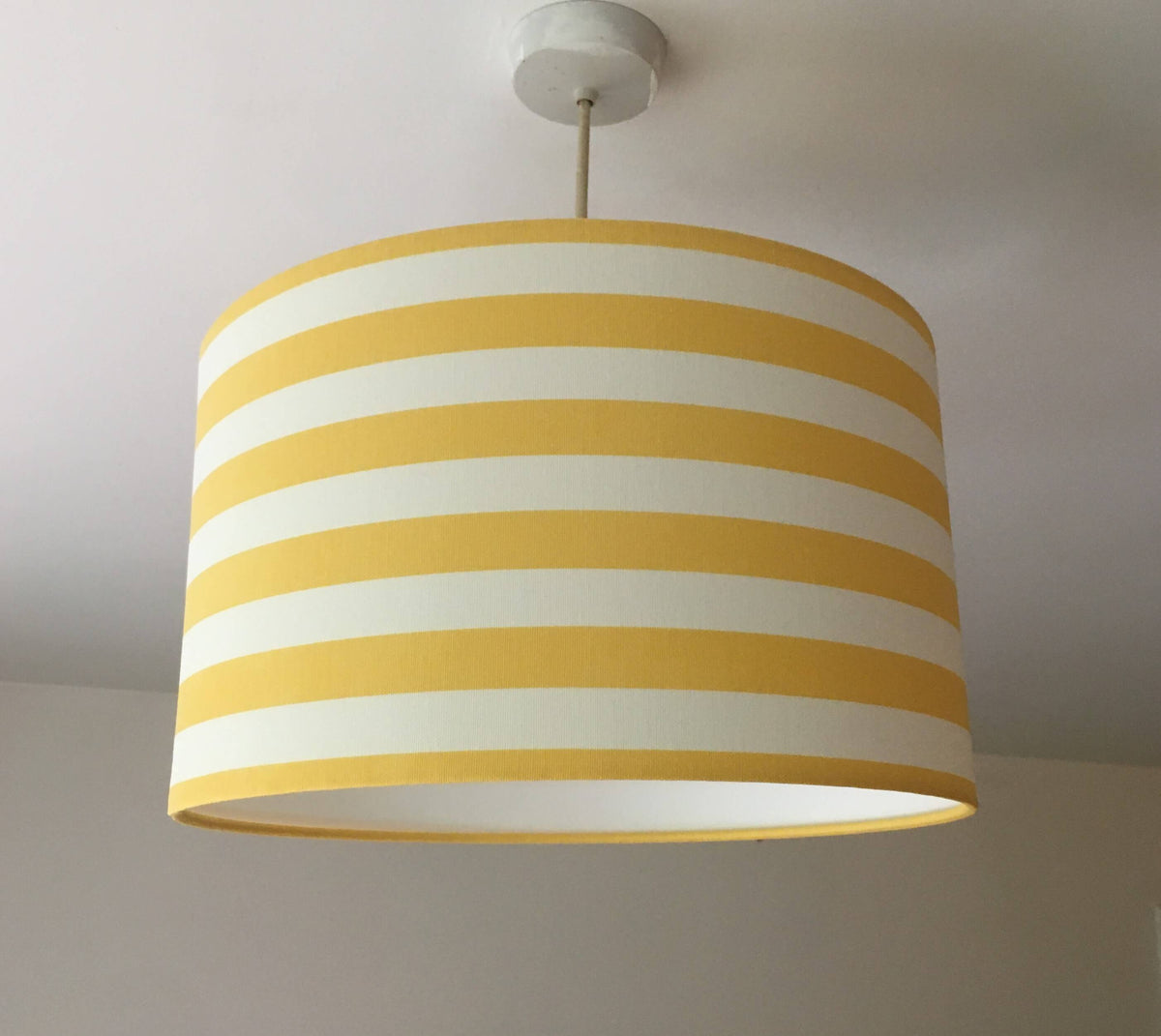 Yellow and white contemporary striped lampshade hanging from a ceiling.
