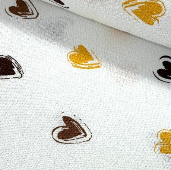 Close-up of cotton double gauze muslin fabric with heart prints in brown and yellow on a white background.