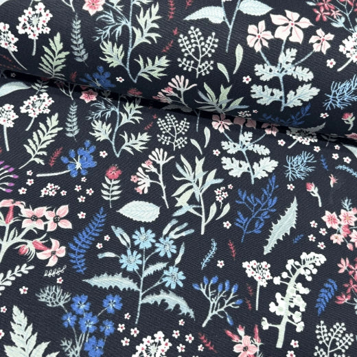 Floral patterned upholstery curtain fabric with various wild flowers in pink and blue and green leaves on a dark background.