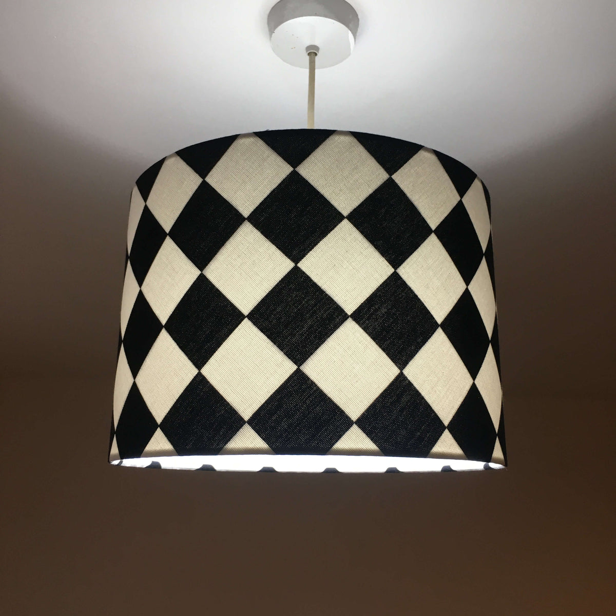 Geometric checkered lampshade with black and white pattern on a plain background with lights on.