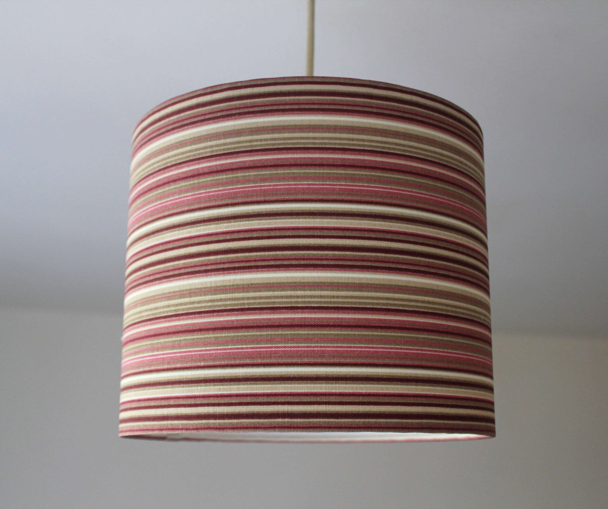 Striped ceiling lampshade with pink, burgundy and beige pattern on a plain background.