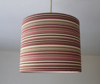 Striped ceiling lampshade with pink, burgundy and beige pattern on a plain background.