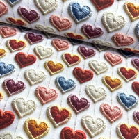 Colorful embroidered hearts on a white upholstery fabric background.