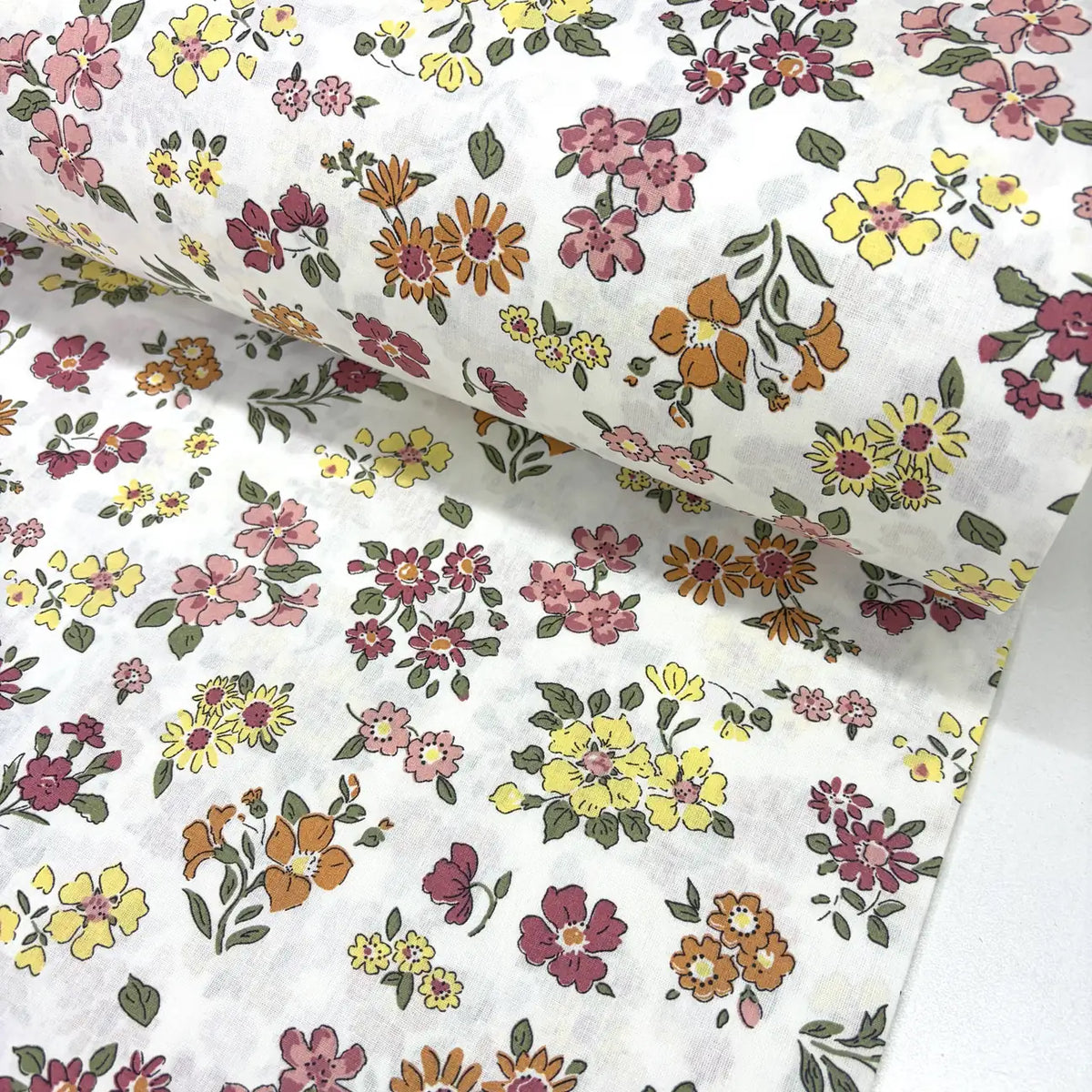 Floral cotton fabric patterned with blush pink, terracotta, yellow and burgundy flowers on a white background.