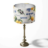 Decorative table lampshade featuring yellow lemons, green leaves, black olives and blue ornaments on a white background.