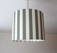 Striped ceiling lampshade with grey and white vertical stripes on a plain background.