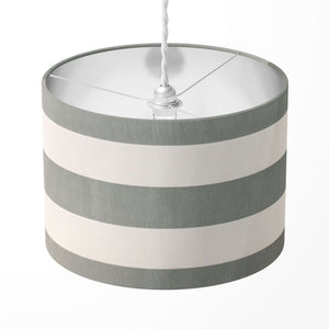 A cylindrical drum lampshade featuring horizontal stripes in varying shades of grey and white. 