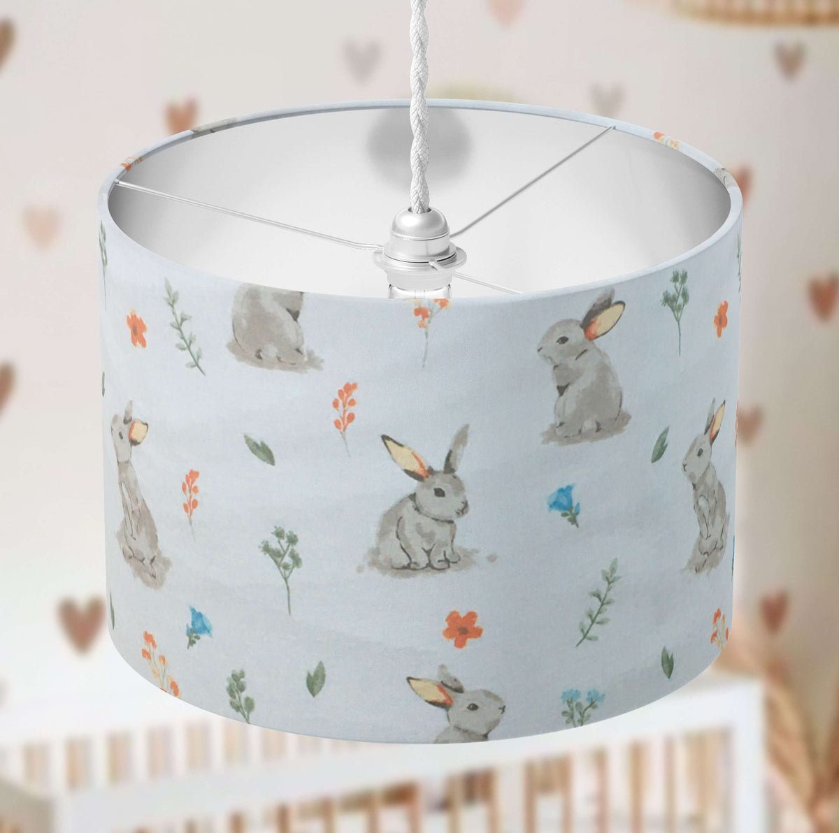 Bunny print kids room drum lampshade in beige, orange, green, blue and white on a blurred background.