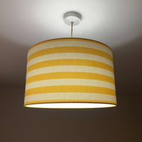 Ceiling light shade with a yellow and white stripe pattern on a plain background.