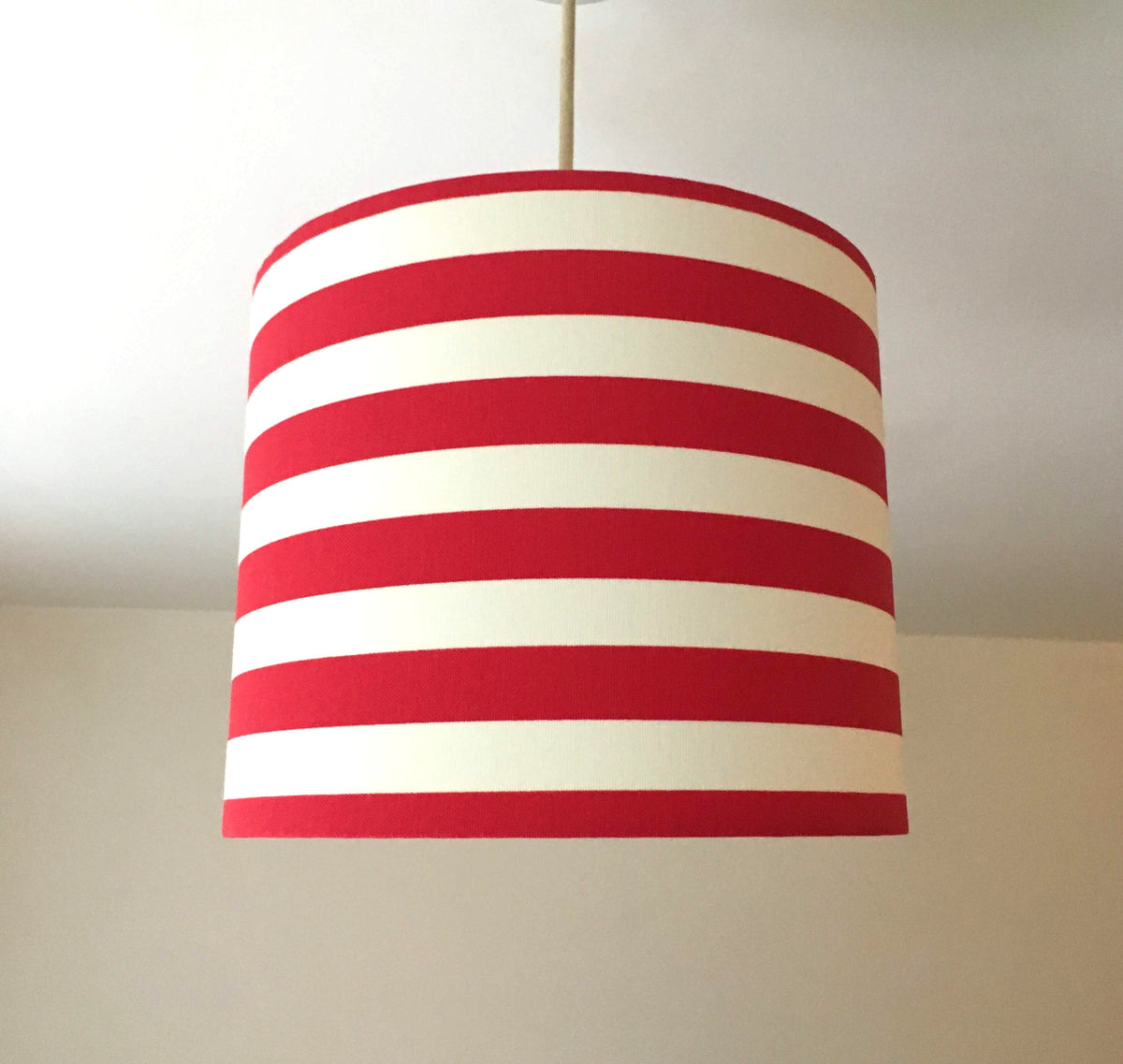 Striped red and white ceiling lampshade hanging against a plain background.