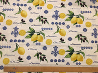Upholstery fabric printed with yellow lemon, black olive, green leaves and blue ornaments on a white background.
