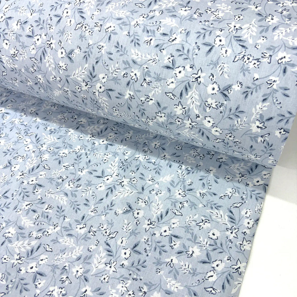 Floral patterned fabric with small white flowers on a light blue background.