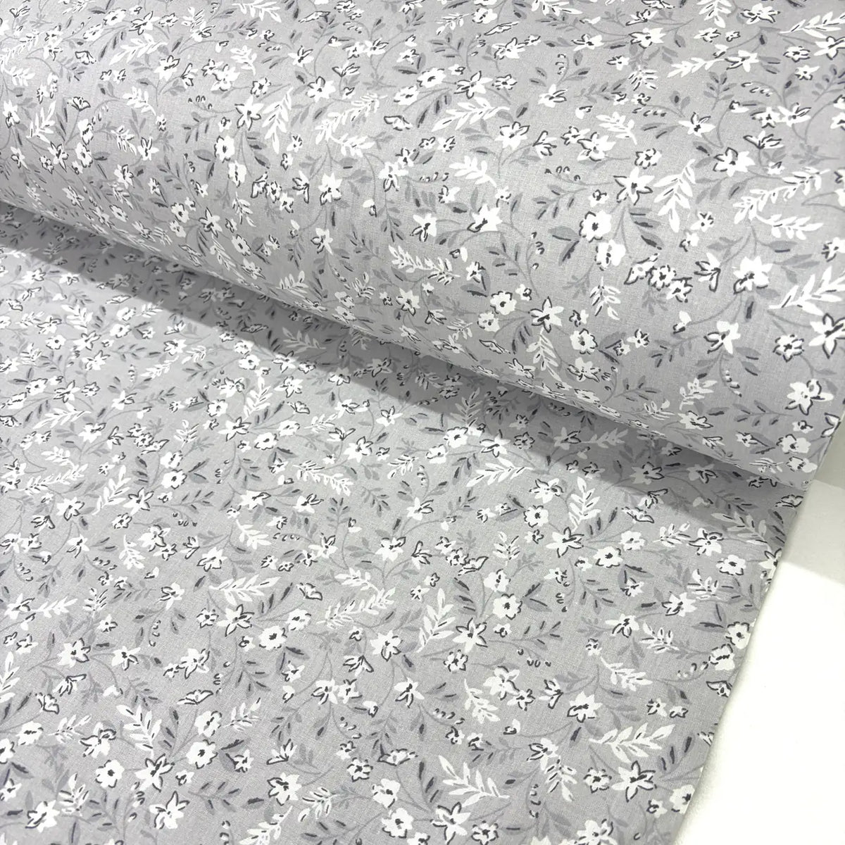 Light grey ditsy floral fabric patterned with small white flowers on a sliver grey background.