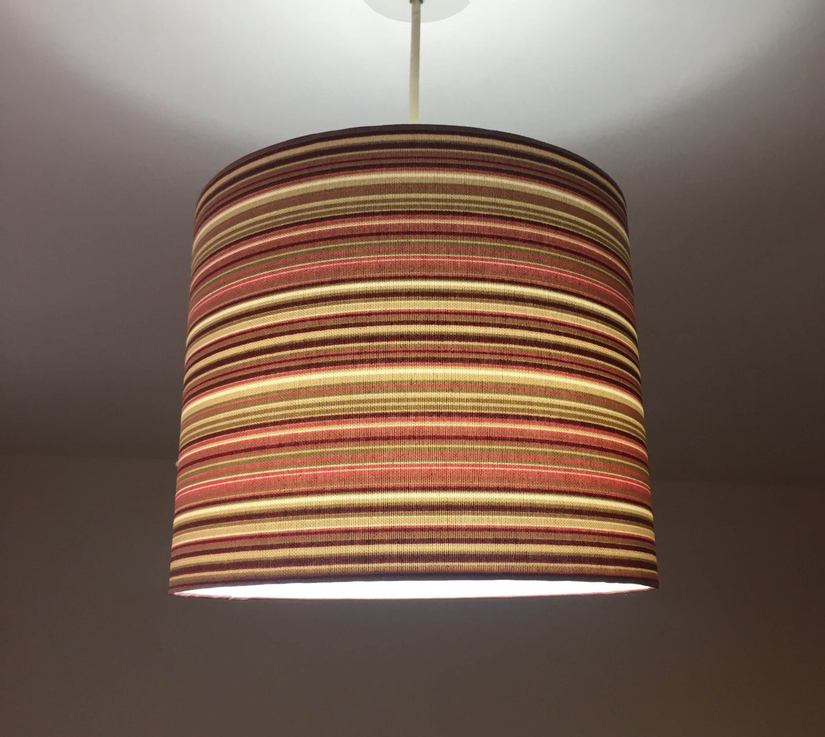 Pink striped lampshade hanging against a plain background.