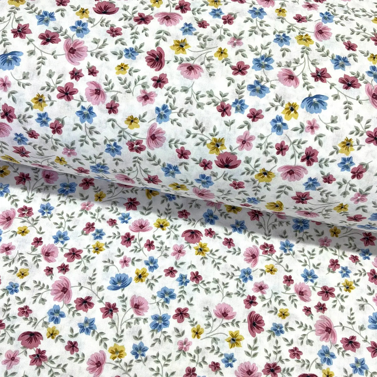 Multicolour ditsy floral cotton fabric patterned with small pink, blue, mustard yellow and burgundy flowers on a white background.
