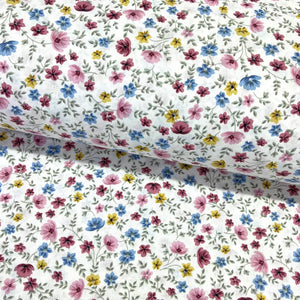 Multicolour ditsy floral cotton fabric patterned with small pink, blue, mustard yellow and burgundy flowers on a white background.