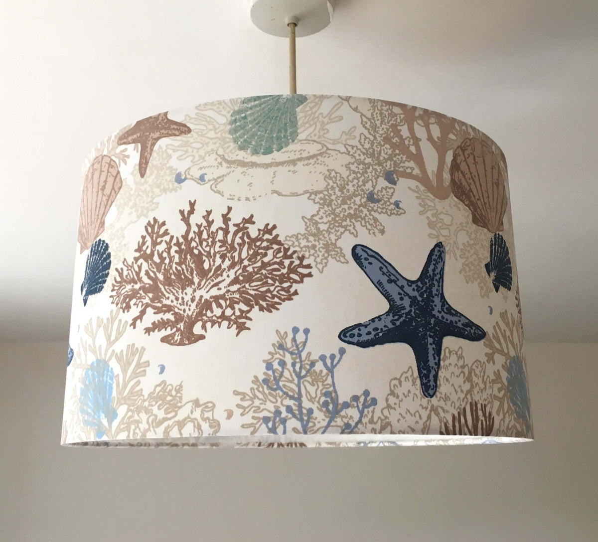 Beige ceiling lampshade patterned with ocean, sea shells, reefs and starfishes.