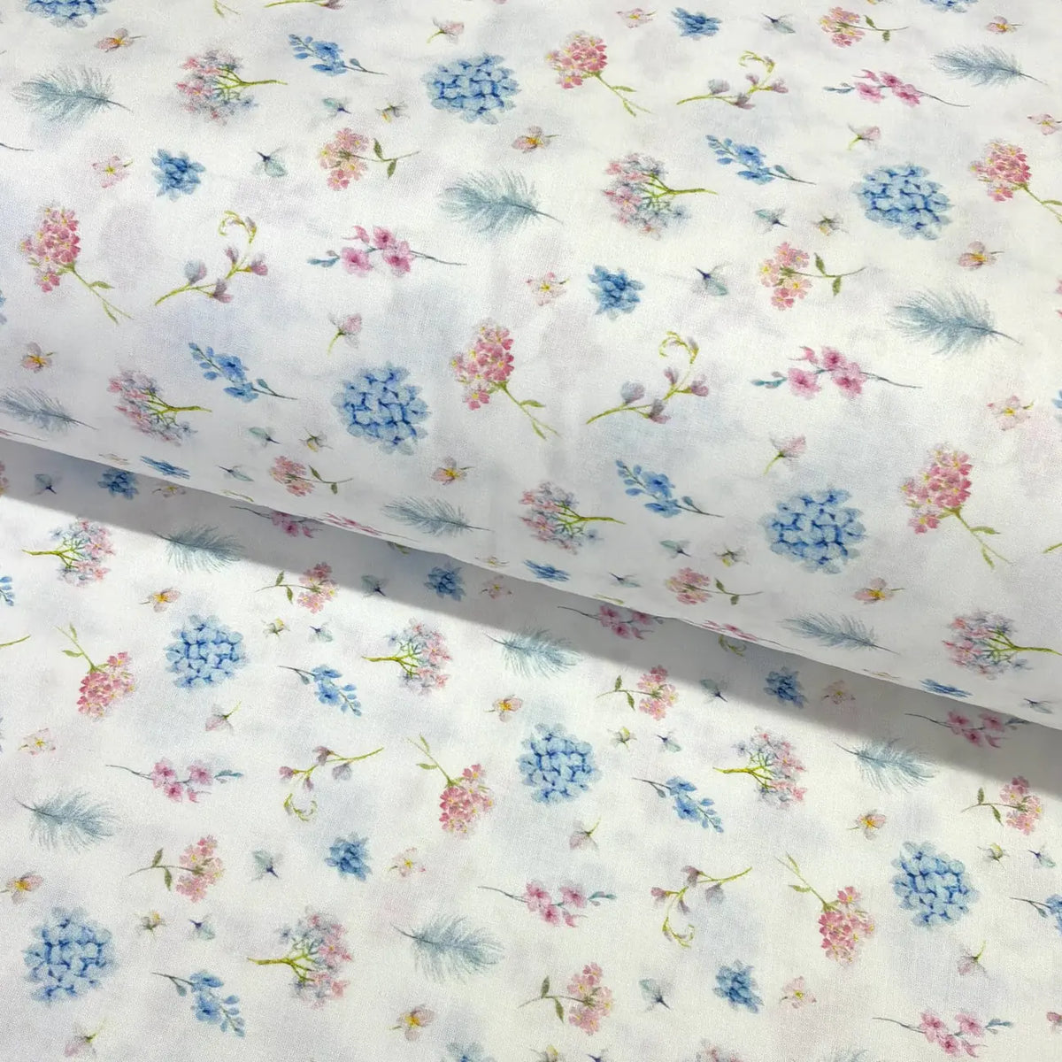 Pastel ditsy floral cotton fabric featuring delicate blue and pink flowers with botanical sprigs on a white background.