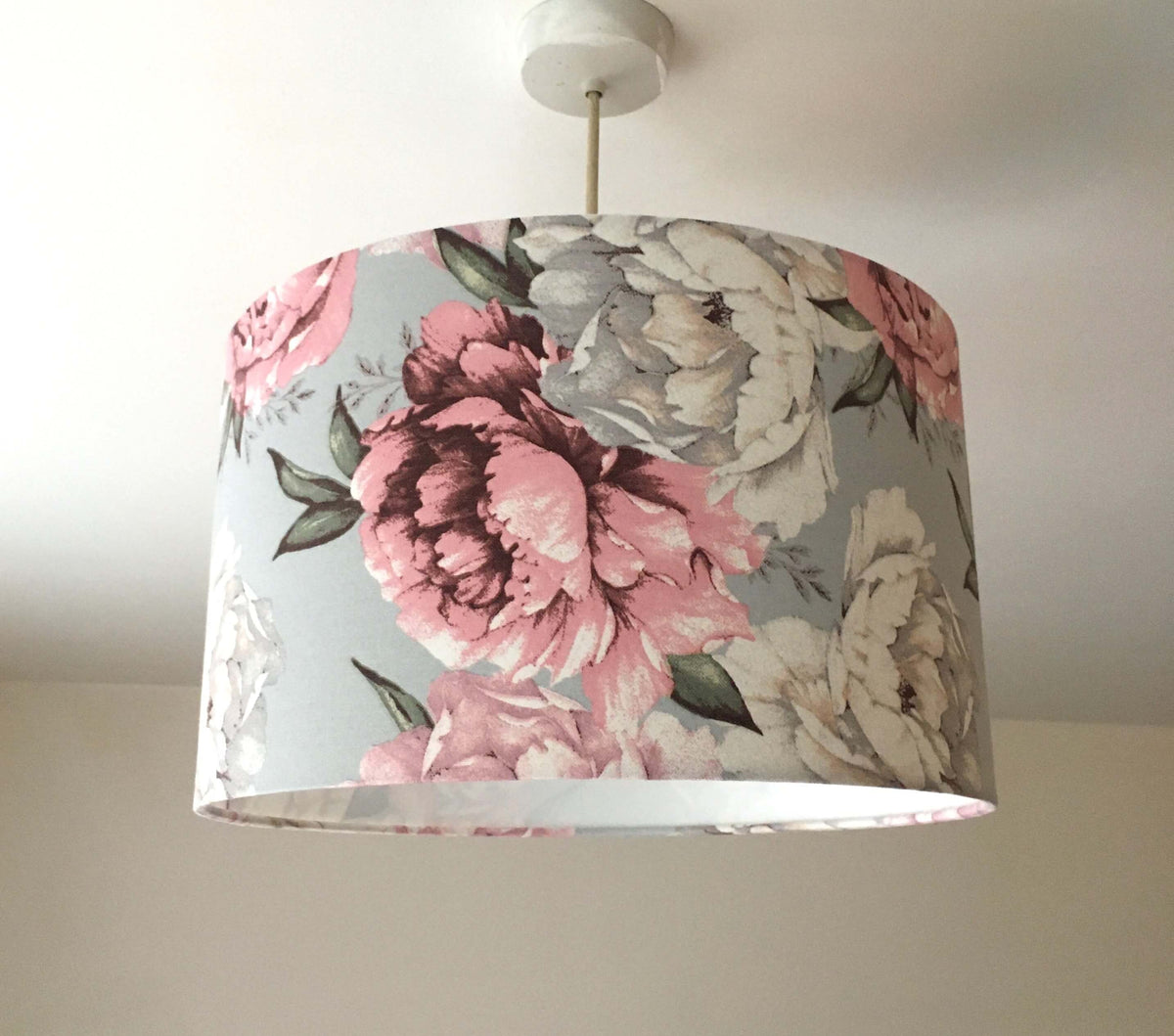 Peony flower patterned lampshade in  light pink, white and grey hanging against a neutral background.