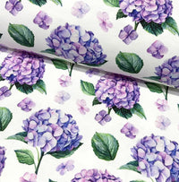 Fabric patterned with lilac hydrangea flowers and green leaves on a white background.