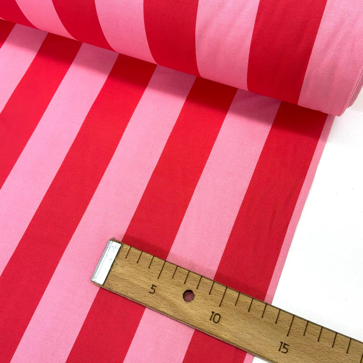 Roll of red and pink striped fabric with a wooden ruler for scale.