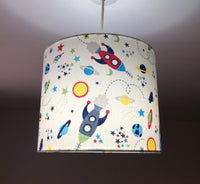 Nursery room lampshade with space-themed design featuring rockets, planets, and stars on a beige background.
