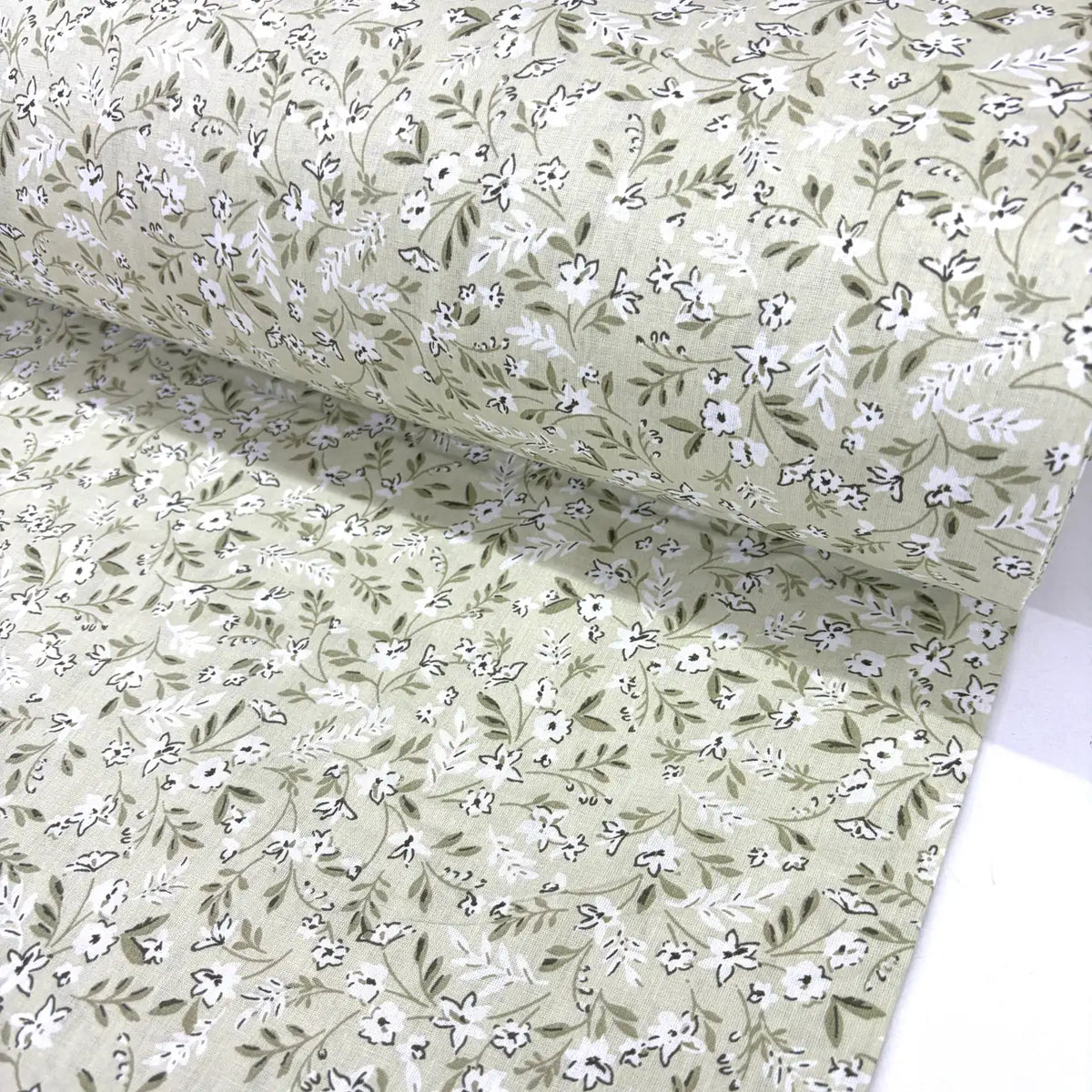 Floral patterned fabric with small white flowers and green leaves on a light sage green background.