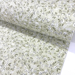 Floral patterned fabric with small white flowers and green leaves on a light sage green background.