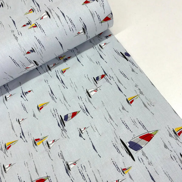 A roll of light gray fabric with a repeating print of small sailboats in red, yellow, blue, and white, alongside abstract black brushstroke lines.