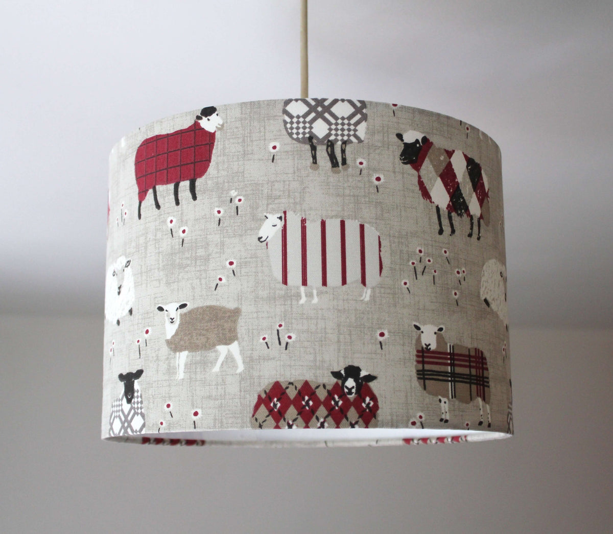 Ceiling lampshade with grey, beige and red sheep pattern on a plain background.