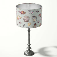 Silver grey table lampshade with pink beach shell patterns on a white background.