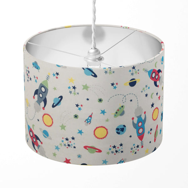 A children's lampshade with a space-themed pattern featuring rockets, planets, sun and stars, displayed on a white background.
