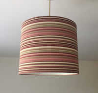 Rose pink, burgundy, brown and cream striped lampshade hanging from a ceiling on a plain background.