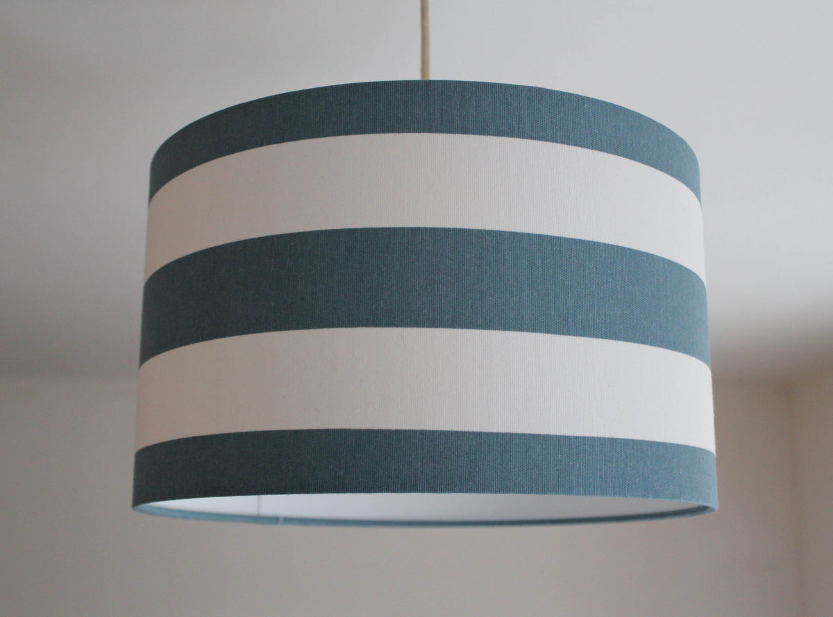 Horizontal striped lampshade with teal blue and white stripes hanging from a ceiling.