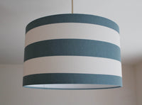 Horizontal striped lampshade with teal blue and white stripes hanging from a ceiling.