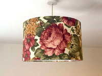 Large red flowers and roses and green leaves patterned lampshade hanging from a ceiling fixture.